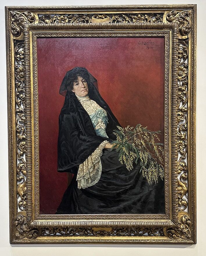 Mimozalı Kadın
1906’da tamamlanan Mimozalı Kadın portresi, Osman Hamdi Bey’in eşi Marie’yi (sonradan Naile adını alan) resmettiği bir eserdir. İstanbul Resim Ve Heykel Müzesi’nde sergilenen tablo, batılı üslubuyla dikkat çeker. Mimozaların zarif dokunuşu ve Marie’nın duruşu, esere duygusal bir derinlik katar, ressamın eşine duyduğu sevgiyi yansıtır.